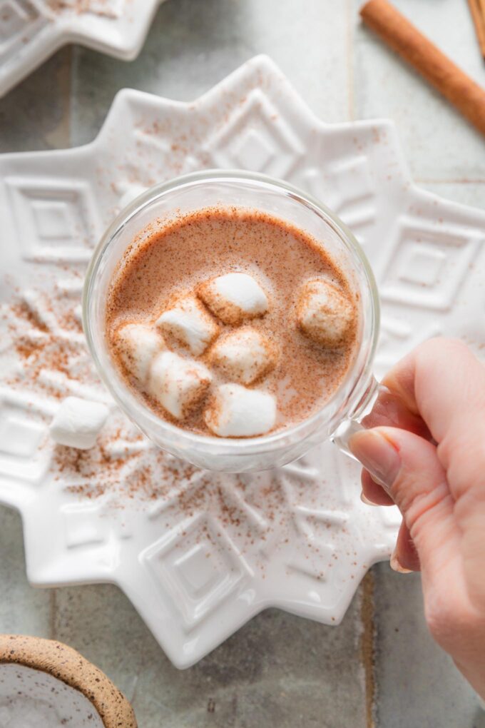 Woman's hand holding a small mug of spiced hot cocoa with marshmallows.