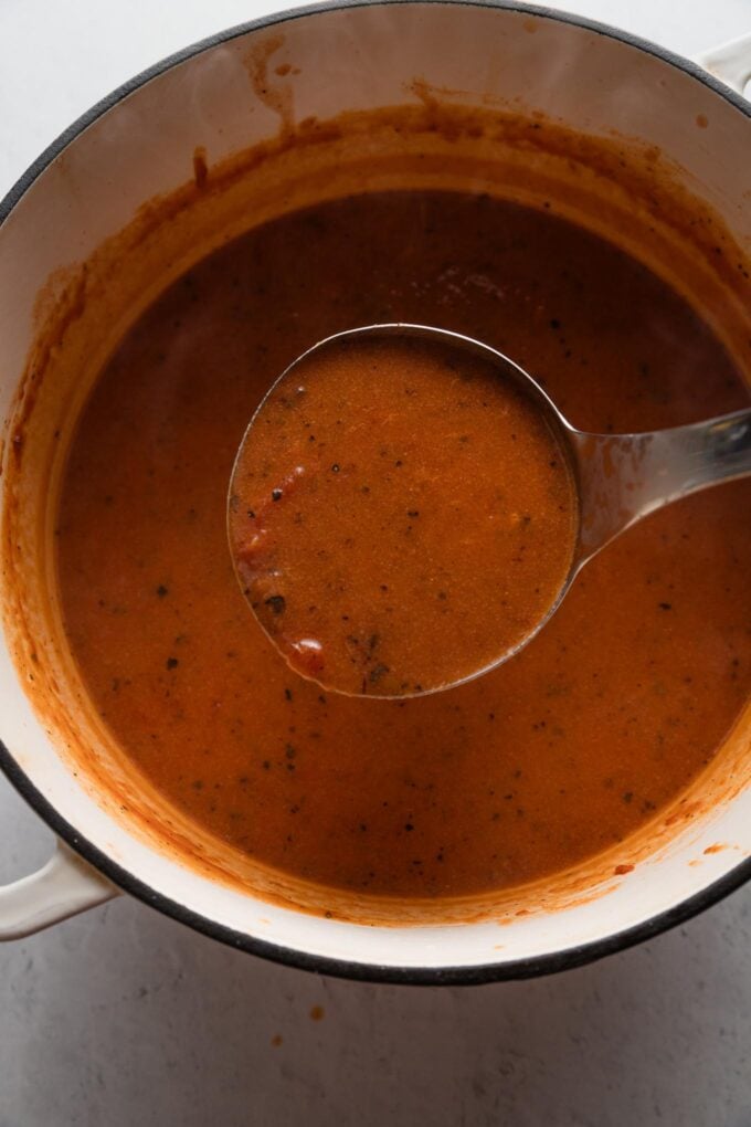 Ladle full of 20-minute tomato soup over a Dutch oven.