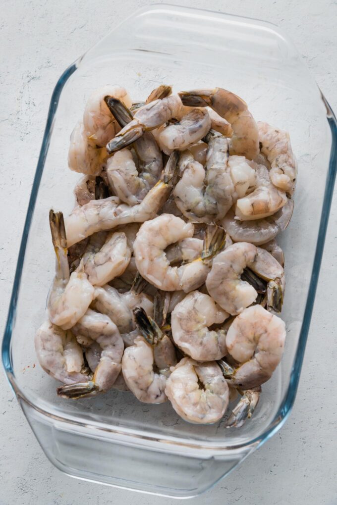 Uncooked, thawed shrimp tossed in a small glass baking dish.
