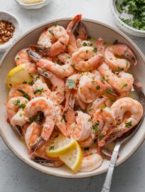Bowl full of oven-baked shrimp with lemon garlic butter sauce, fresh parsley, and red pepper flakes.