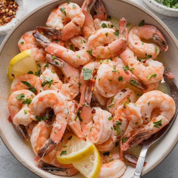 Bowl full of oven-baked shrimp with lemon garlic butter sauce, fresh parsley, and red pepper flakes.
