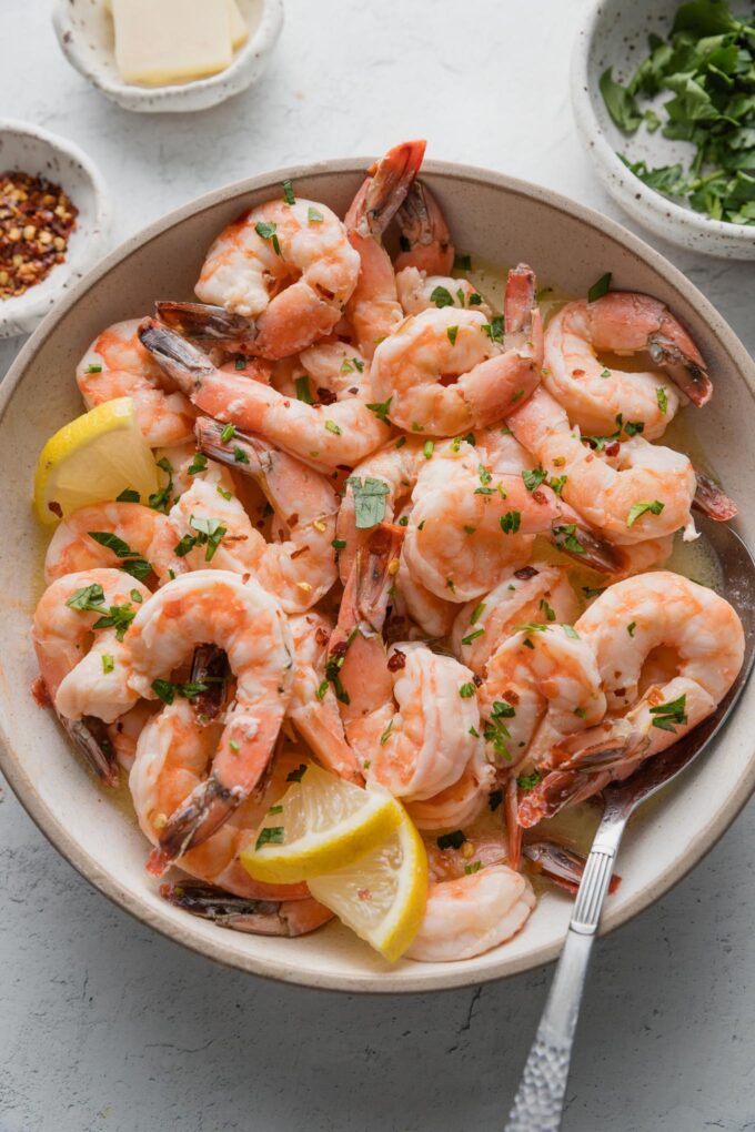 Bowl full of oven-baked shrimp with lemon garlic butter sauce, fresh parsley, and red pepper flakes.