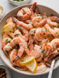 Angled view of a bowl full of oven-baked lemon garlic shrimp sprinkled with parsley and red pepper flakes.