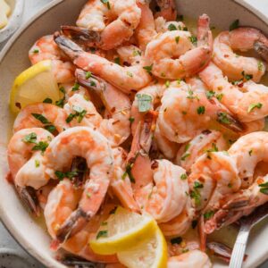 Angled view of a bowl full of oven-baked lemon garlic shrimp sprinkled with parsley and red pepper flakes.