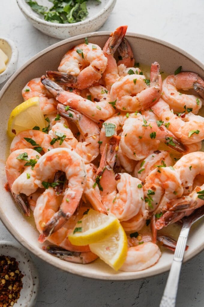 Angled view of a bowl full of oven-baked lemon garlic shrimp sprinkled with parsley and red pepper flakes.