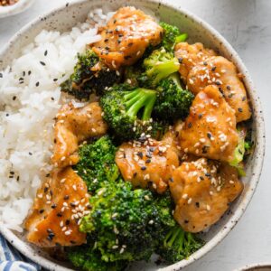 Bowl of Asian chicken and broccoli with rice and sesame seeds.