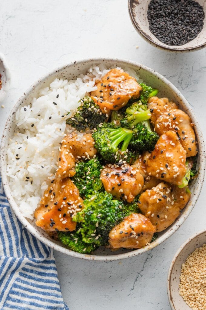 Bowl of chicken and broccoli stir fry served with jasmine rice and sesame seeds.