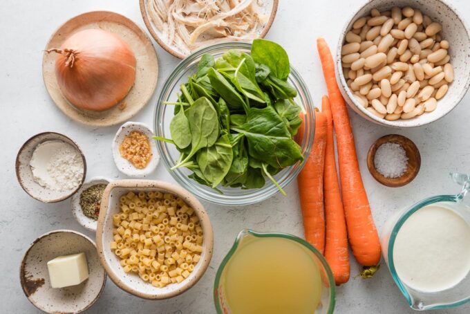 Overhead image of the ingredients for a chicken soup with cream, a light roux, carrots, spinach, onions, pasta, and white beans.
