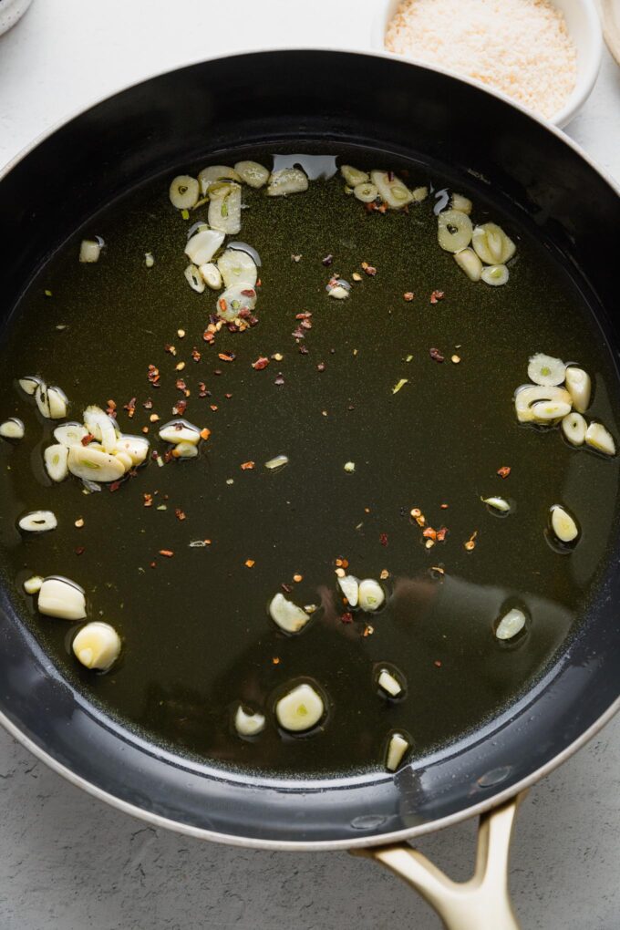 Thinly-sliced garlic cloves simmering in olive oil.