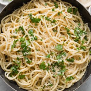 Large skillet full of spaghetti aglio e olio with fresh Parmesan and minced parsley.