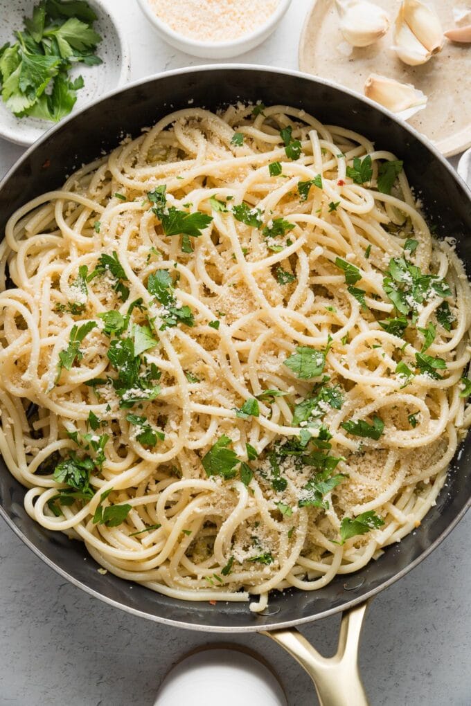 Large skillet full of spaghetti aglio e olio with fresh Parmesan and minced parsley.