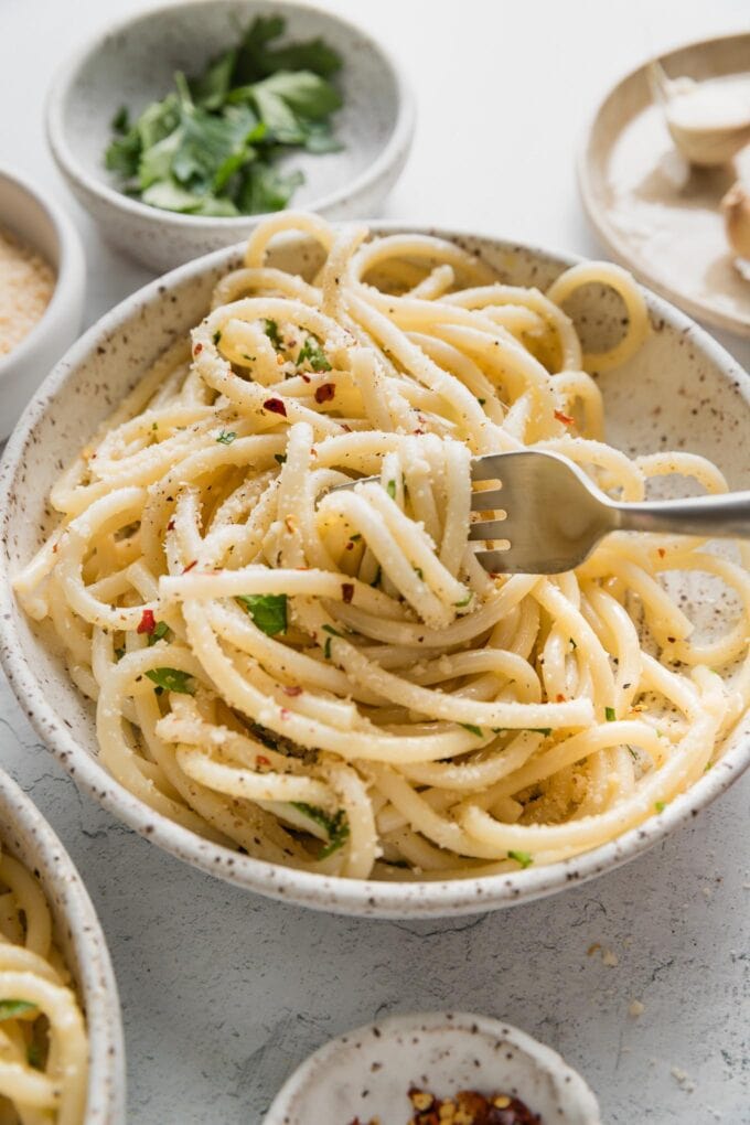 Fork twirling a big spiral of spaghetti aglio e olio from a small ceramic pasta bowl.