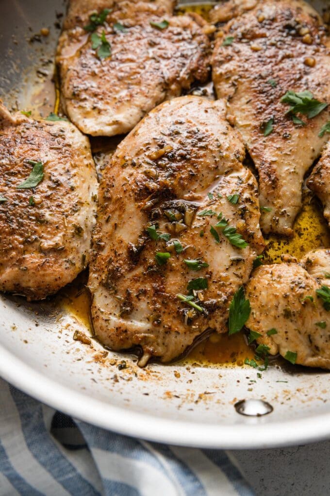 Stainless steel skillet filled with garlic herb butter chicken breasts.