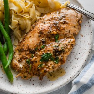 Dinner plate with a garlic butter chicken breast, green beans, and egg noodles.