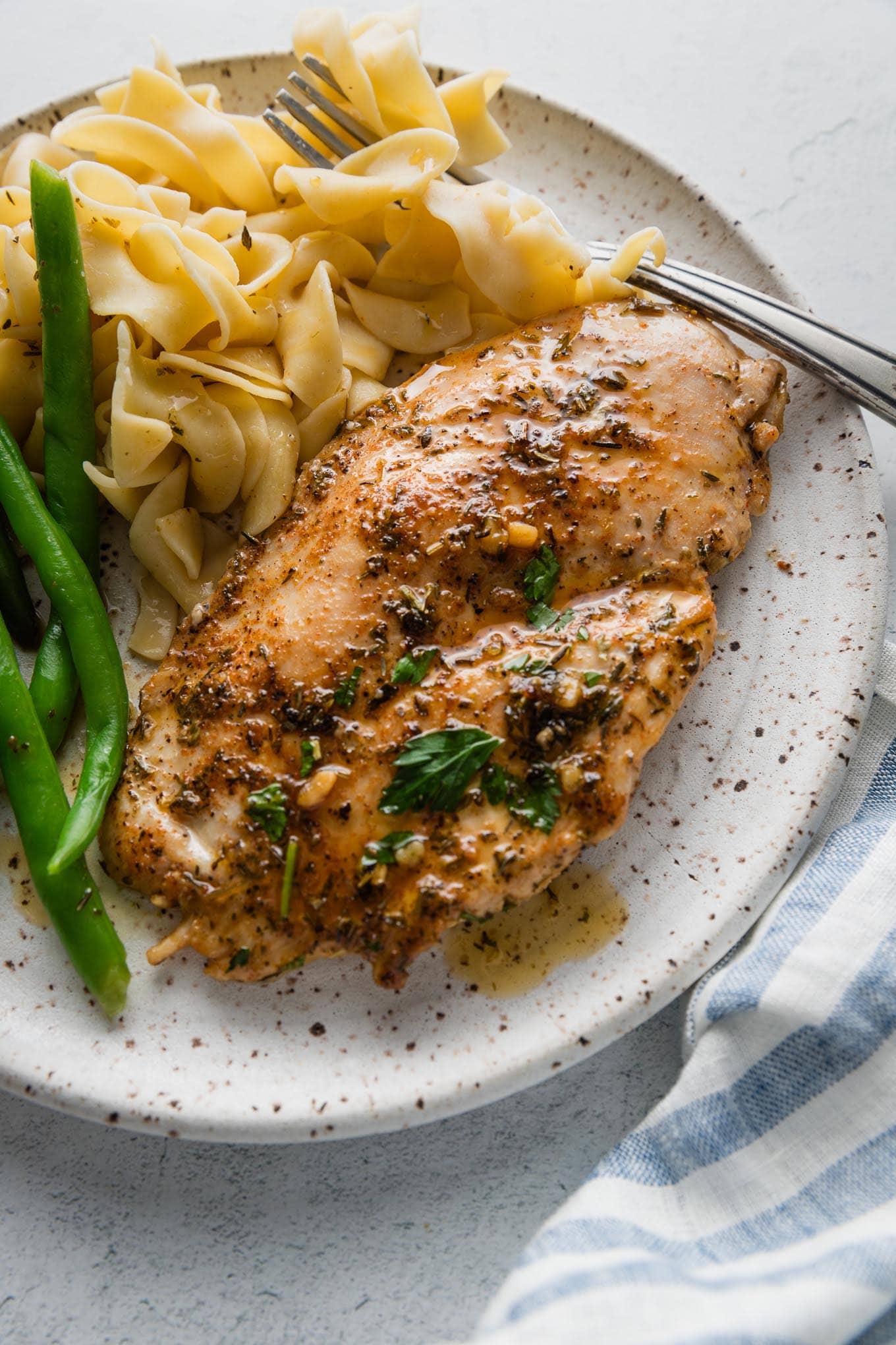 Dinner plate with a garlic butter chicken breast, green beans, and egg noodles.