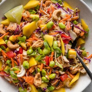 Bowl full of a chopped Thai chicken salad with cabbage, peppers, mango, edamame, cashes, and a sweet chili dressing.