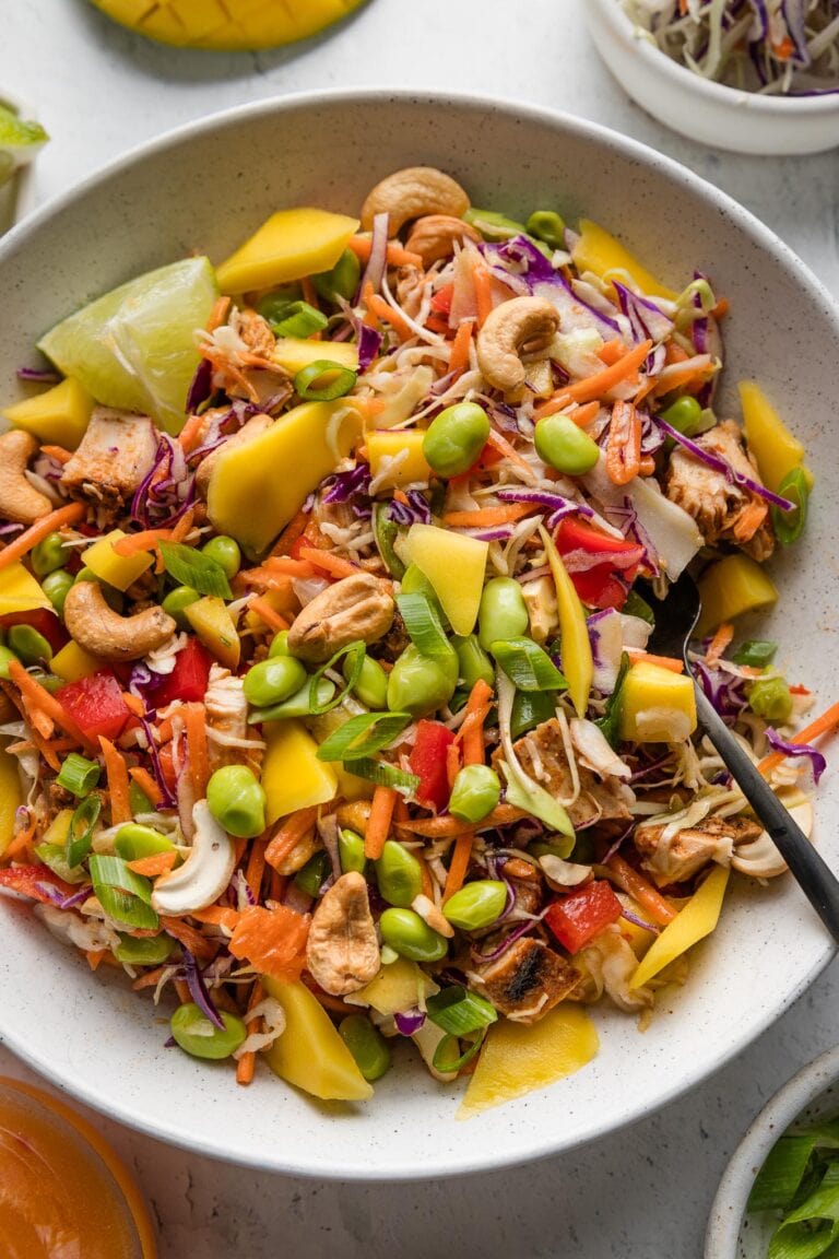 Bowl full of a chopped Thai chicken salad with cabbage, peppers, mango, edamame, cashes, and a sweet chili dressing.