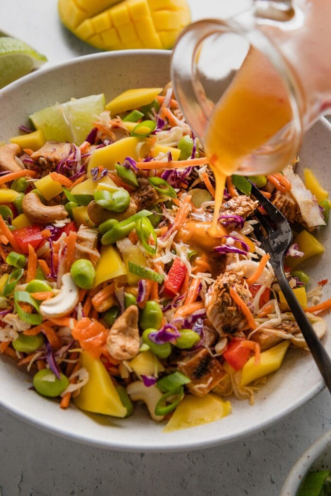 Small glass cruet pouring a translucent, glossy orange sweet chili vinaigrette over a chopped Thai chicken salad.