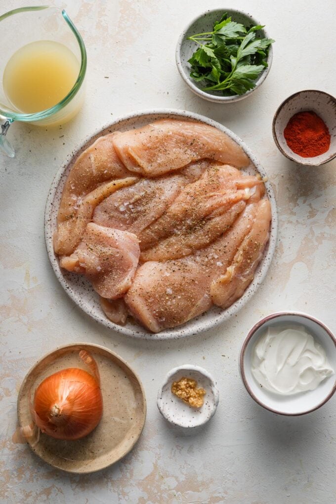 Overhead view of ingredients for paprika chicken: chicken breasts, paprika, garlic, onion, kosher salt, pepper, sour cream.