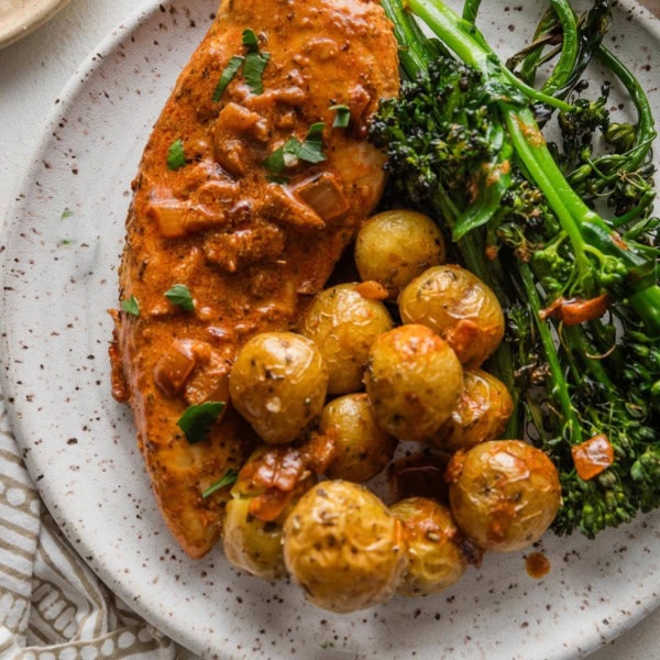 Dinner plate of creamy paprika chicken served with roasted baby potatoes and broccolini.