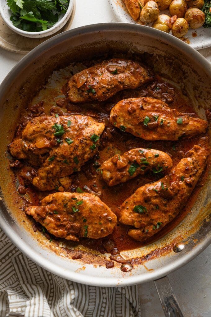 Creamy paprika chicken in a skillet with parsley for garnish.