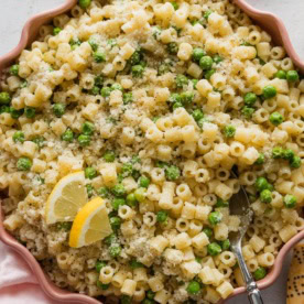Pink scalloped bowl full of ditalini with peas, Parmesan, and lemon zest.