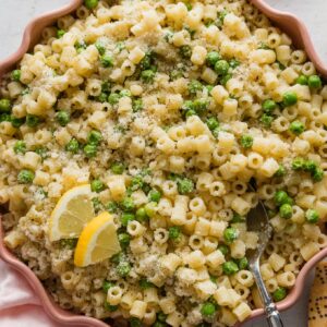 Pink scalloped bowl full of ditalini with peas, Parmesan, and lemon zest.
