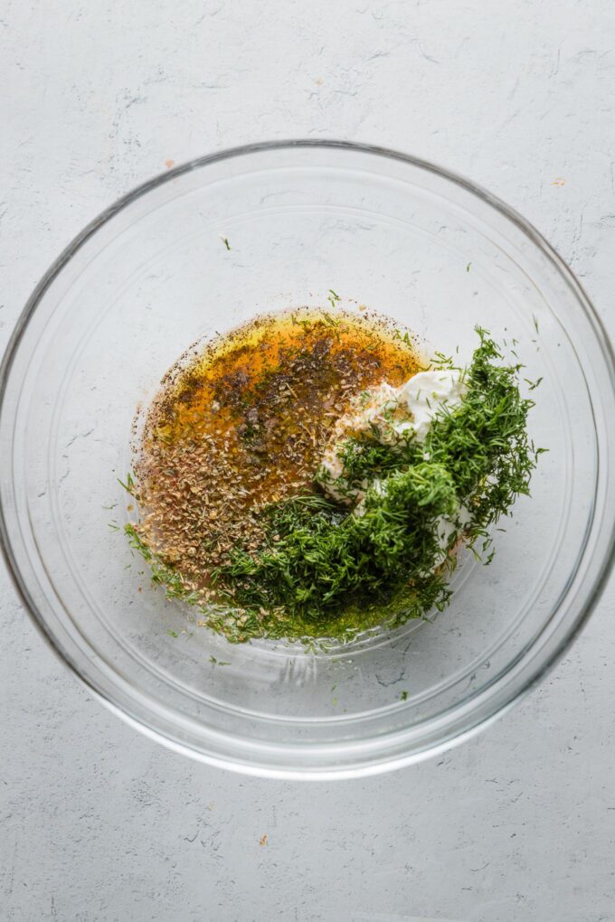 Ingredients for a Mediterranean tuna salad dressing added to a glass prep bowl.