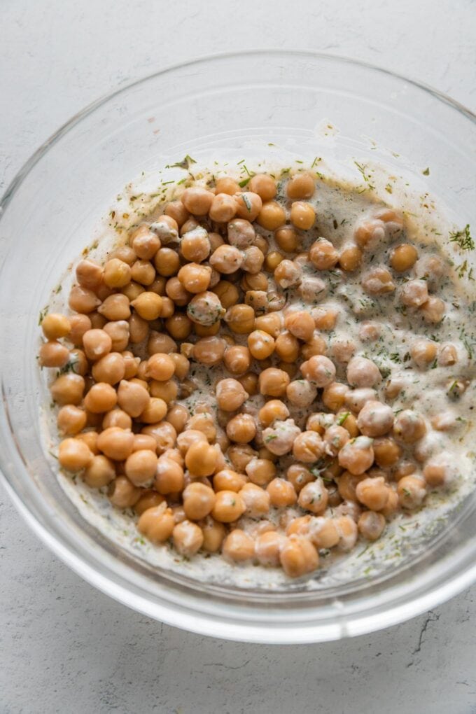 Drained and rinsed chickpeas added to a bowl with a Greek yogurt-based fresh dill dressing.