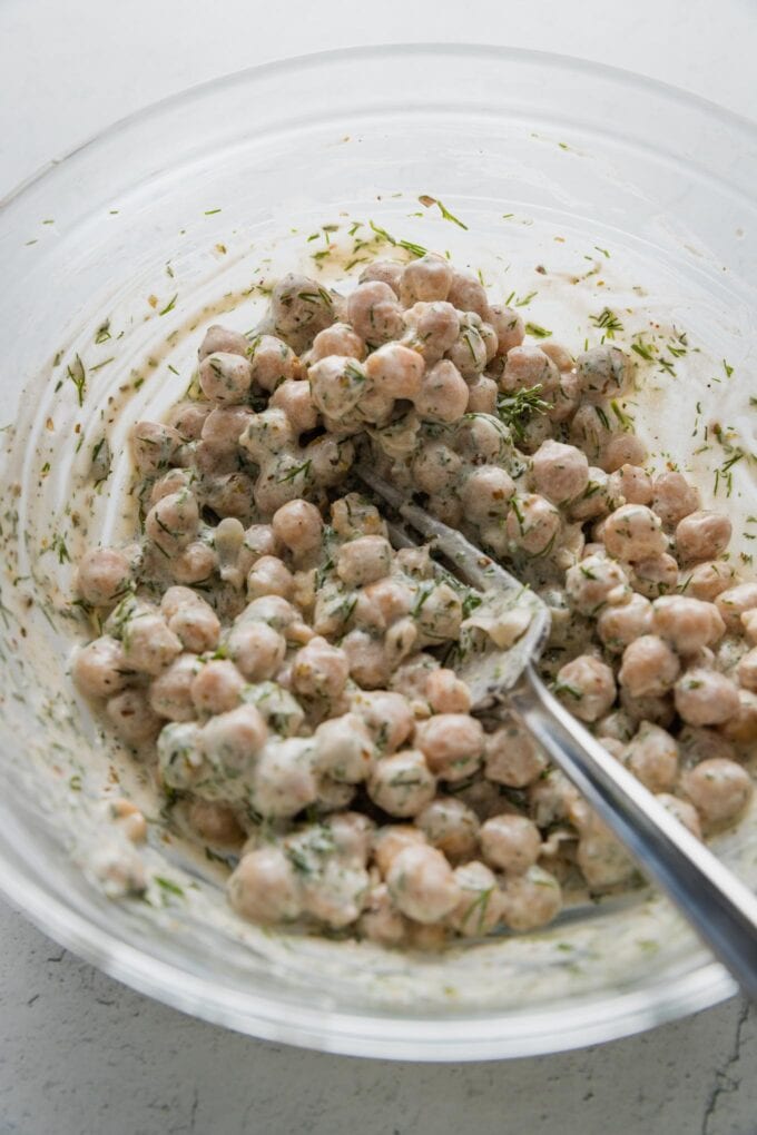 Fork smashing a few chickpeas against the side of the bowl.