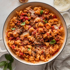 Large enameled skillet full of sausage and peppers pasta.
