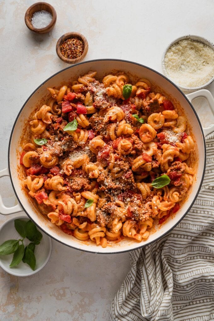 Large enameled skillet full of sausage and peppers pasta.