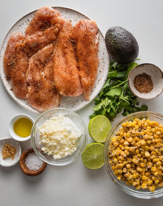 Overhead view of Tajin-seasoned chicken breasts, frozen corn, Cotija, fresh lime, olive oil, garlic, avocado, and cilantro.