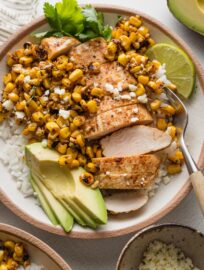 Close up of a rice bowl with Tajin-seasoned chicken breast, street corn with Cotija, avocado, fresh cilantro, and lime.