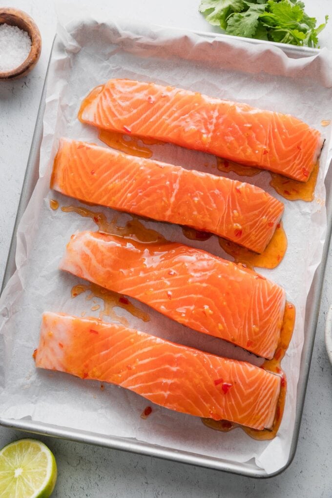 Uncooked salmon filets on a small sheet pan and drizzled with Thai sweet chili sauce.