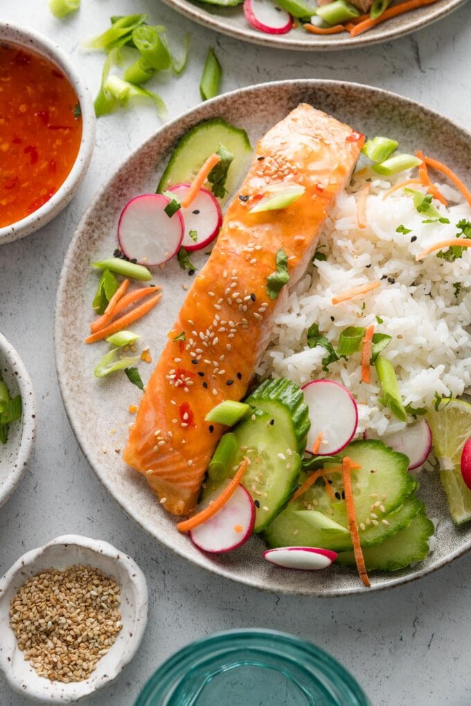 Plate of sweet chili lime salmon served with rice, cucumber, radish, cilantro, lime, and carrots.