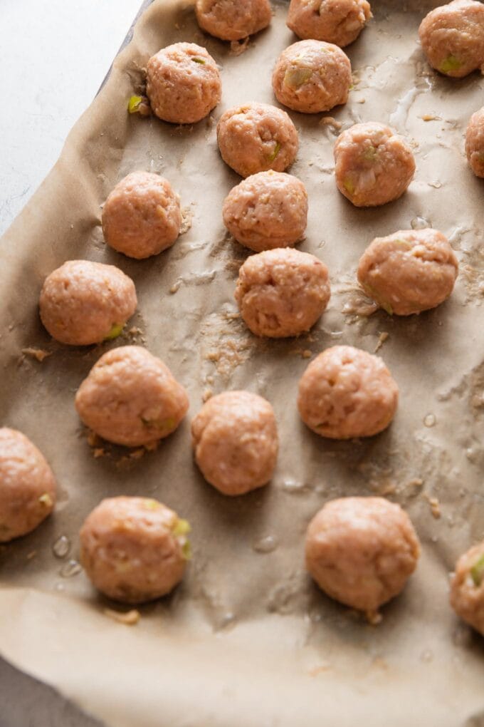 Rolled chicken meatballs ready to bake on a parchment-lined baking tray.