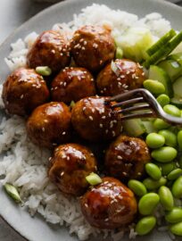 Fork picking up a tender chicken meatball coated in a sweet and sticky Asian-inspired glaze.