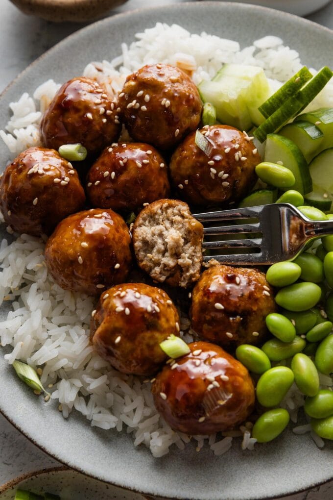 Plate full of Asian inspired chicken meatballs with one cut open to show a really tender, moist interior.