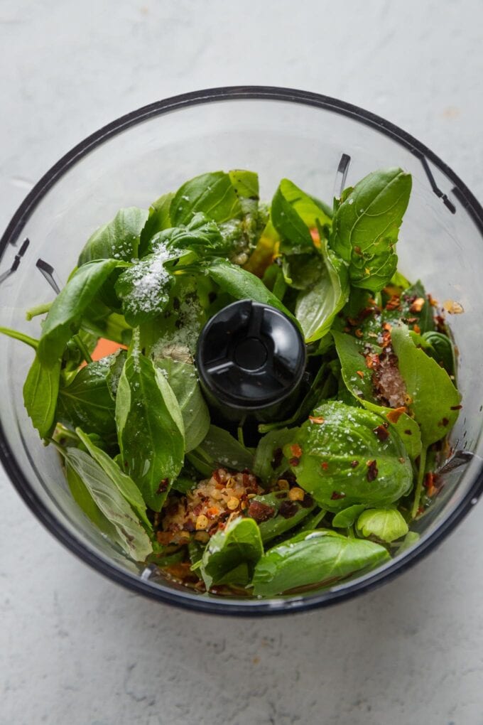 Fresh basil, garlic, and other salad dressing ingredients in the bowl of a small food processor.