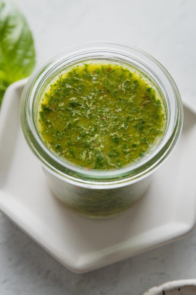 Small glass jar filled with homemade basil vinaigrette.