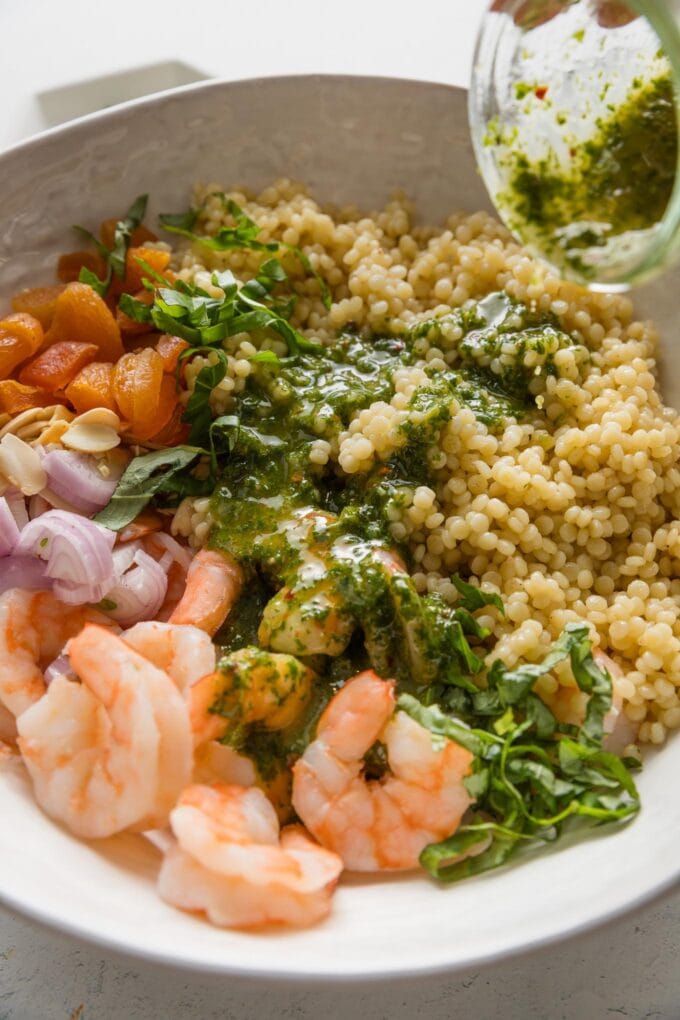 Action shot of basil vinaigrette being poured over poached shrimp and pearl couscous.