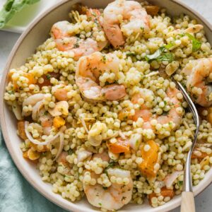 Close up of a bowl of pearl couscous salad with shrimp, dried apricots, slivered almonds, shallots, and fresh homemade basil vinaigrette.