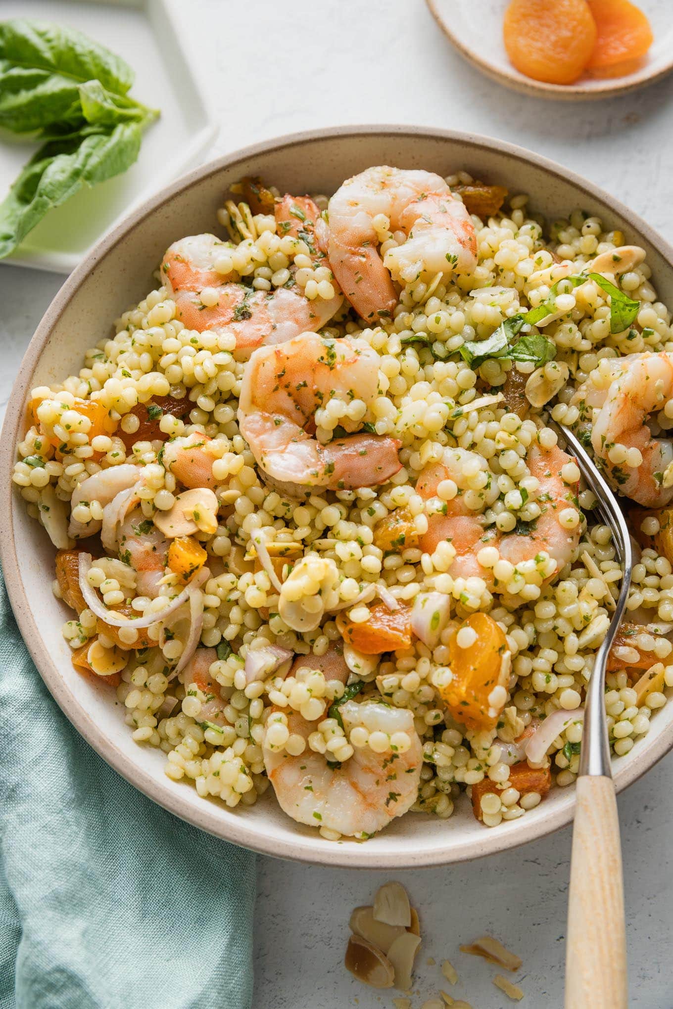 Close up of a bowl of pearl couscous salad with shrimp, dried apricots, slivered almonds, shallots, and fresh homemade basil vinaigrette.