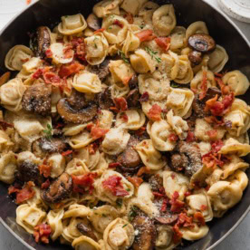 Skillet full of tortellini with bacon, mushrooms, Parmesan, and thyme.