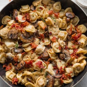 Skillet full of tortellini with bacon, mushrooms, Parmesan, and thyme.