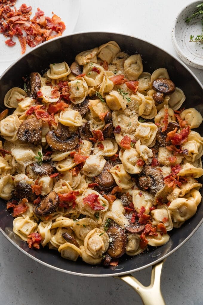 Skillet full of tortellini with bacon, mushrooms, Parmesan, and thyme.