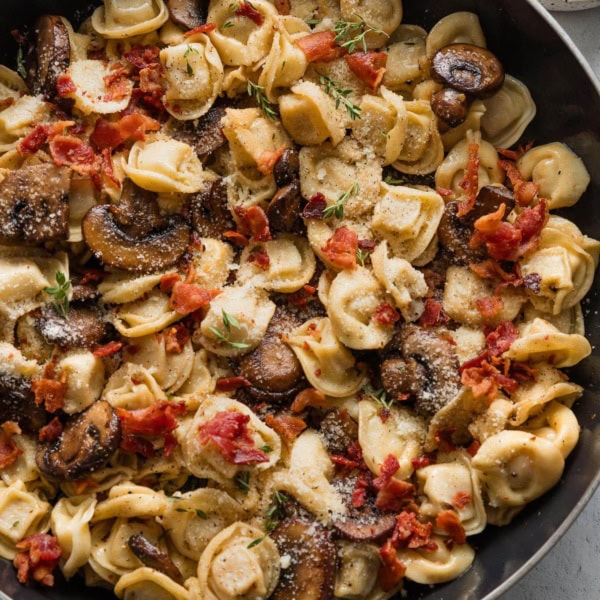 Pan full of tortellini with bacon and mushrooms and thyme.