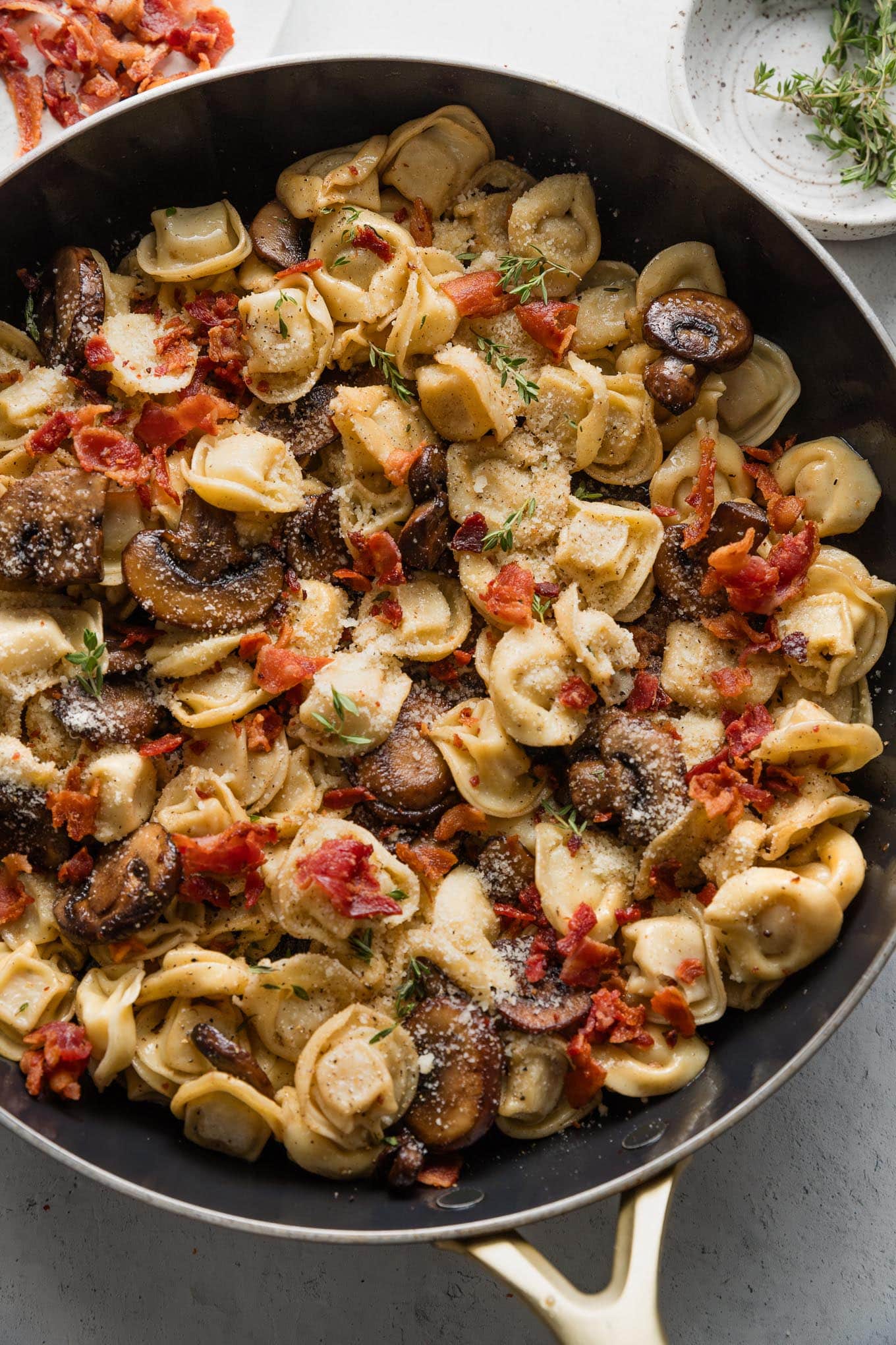 Pan full of tortellini with bacon and mushrooms and thyme.