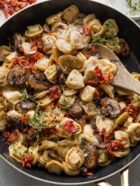 Spoon lifting up a portion of tortellini with mushrooms and bacon.